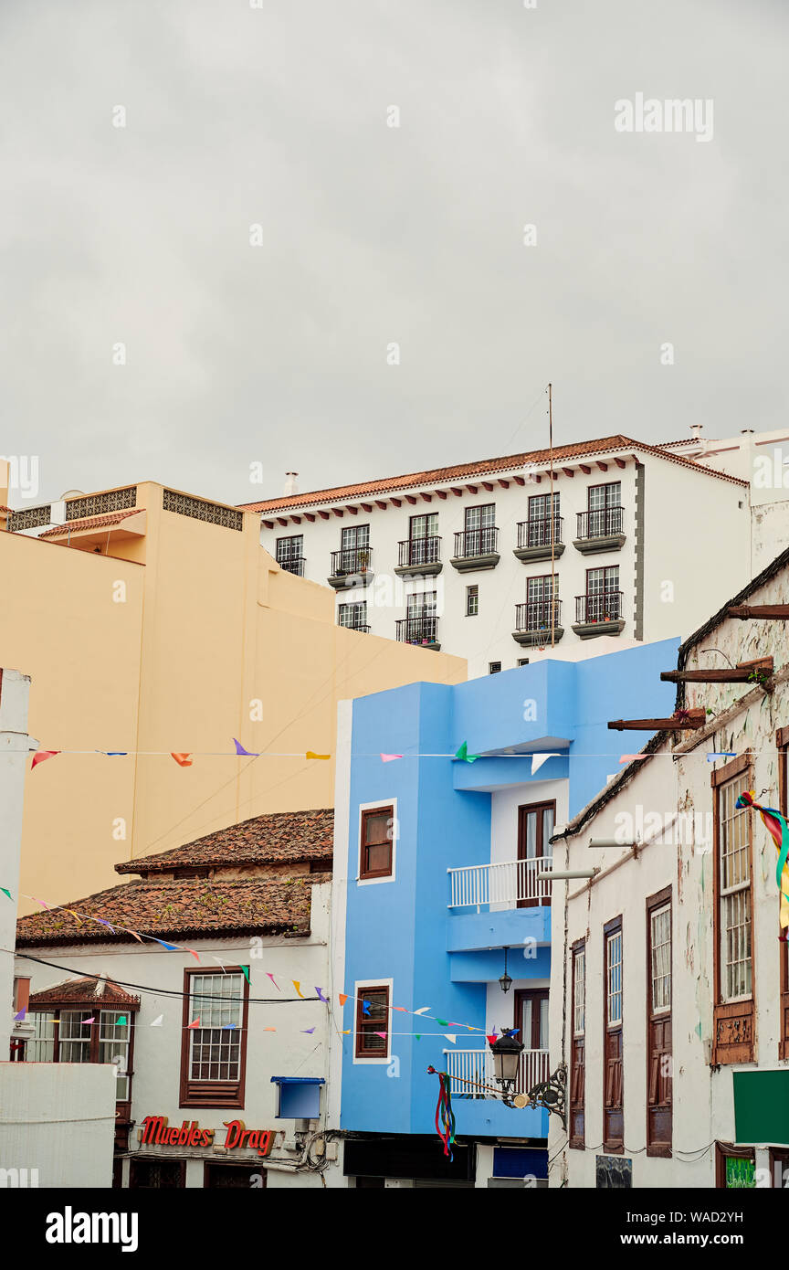 Auténticas casas con techos de tejas y balcones a la calle estrecha decorada con guirnaldas de bandera en Tenerife el día desagradable Foto de stock