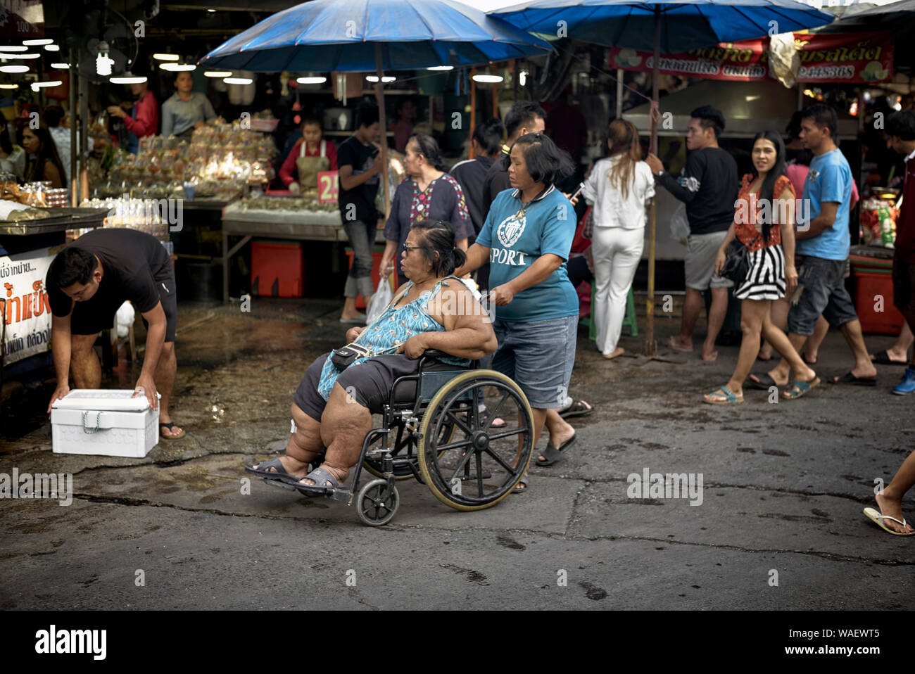 Mujer con Discapacidad con silla de ruedas compras en un mercado callejero  de Tailandia con la ayuda de un asistente Fotografía de stock - Alamy