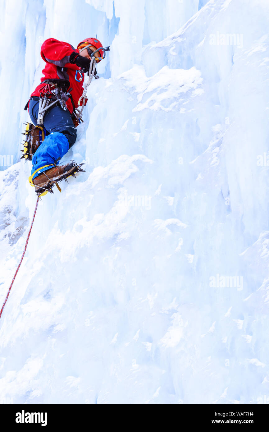 Ice climber preraring ejecutando belay, atornillando el tornillo de hielo en la superficie del glaciar Foto de stock