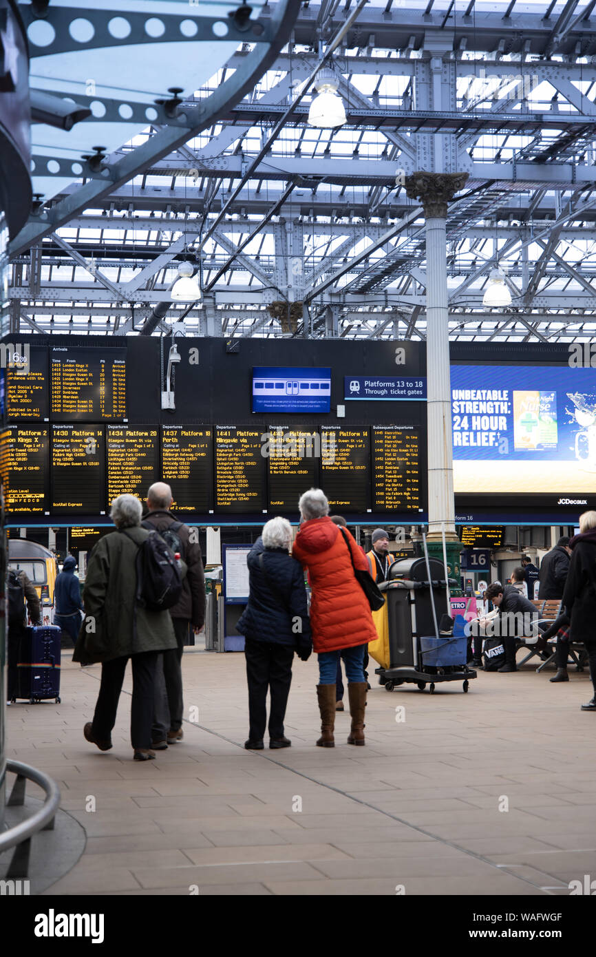 La gente de pie mirando las salidas y las llegadas de pasajeros placas de información de la estación de tren de Waverley en Edimburgo, Escocia, Reino Unido Foto de stock