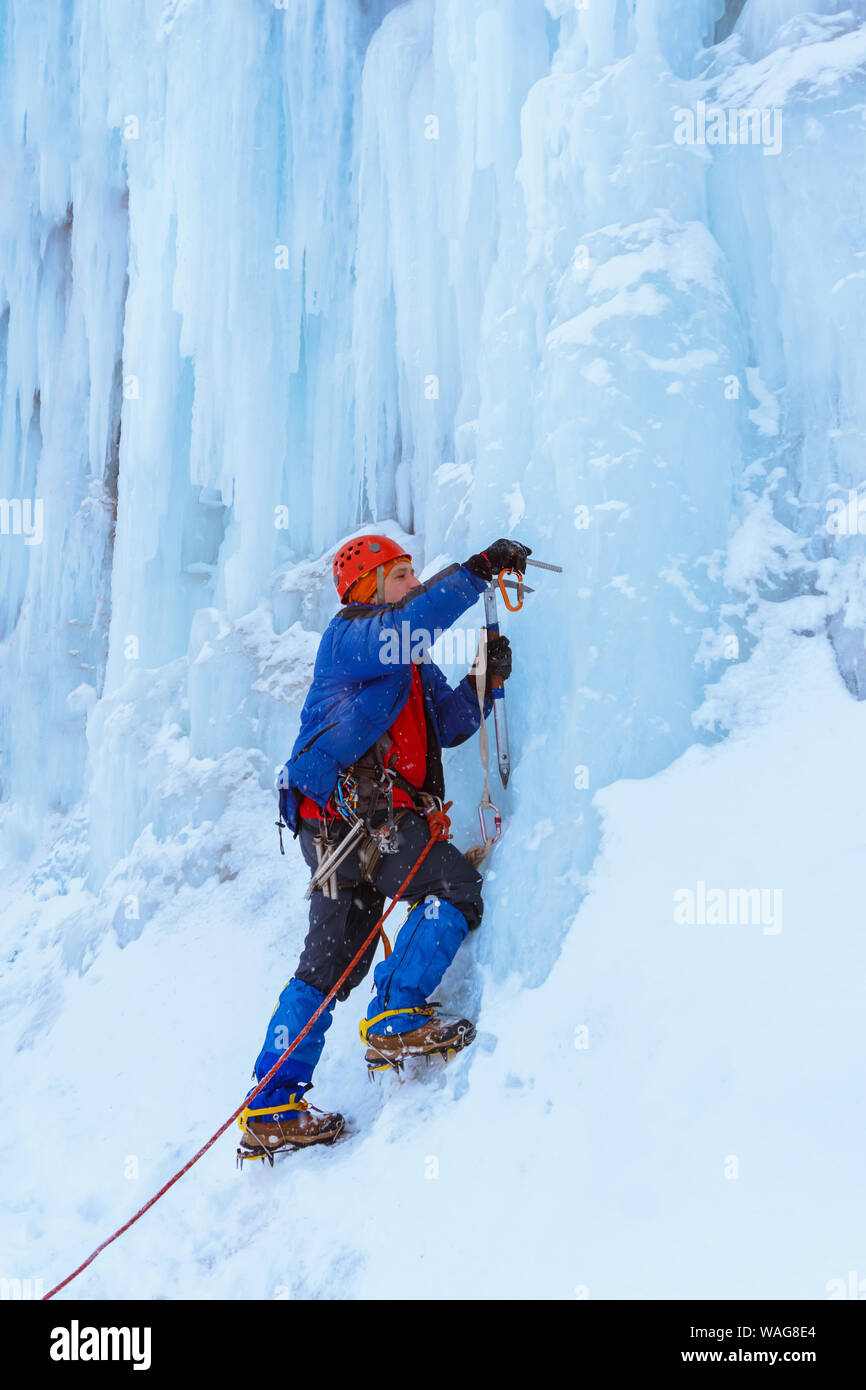 Ice climber preraring ejecutando belay, atornillando el tornillo de hielo en la superficie del glaciar Foto de stock