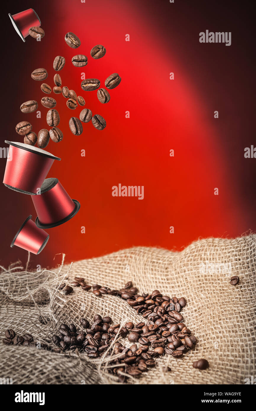 Cápsula de café y granos de café sobre fondo rojo oscuro Foto de stock