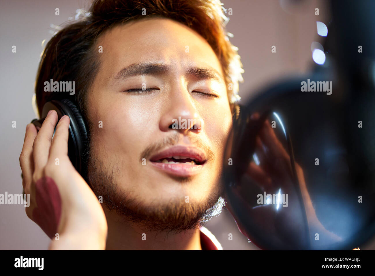 Hombre adulto joven asiático disfrutar cantando una canción en estudio de grabación moderna Foto de stock