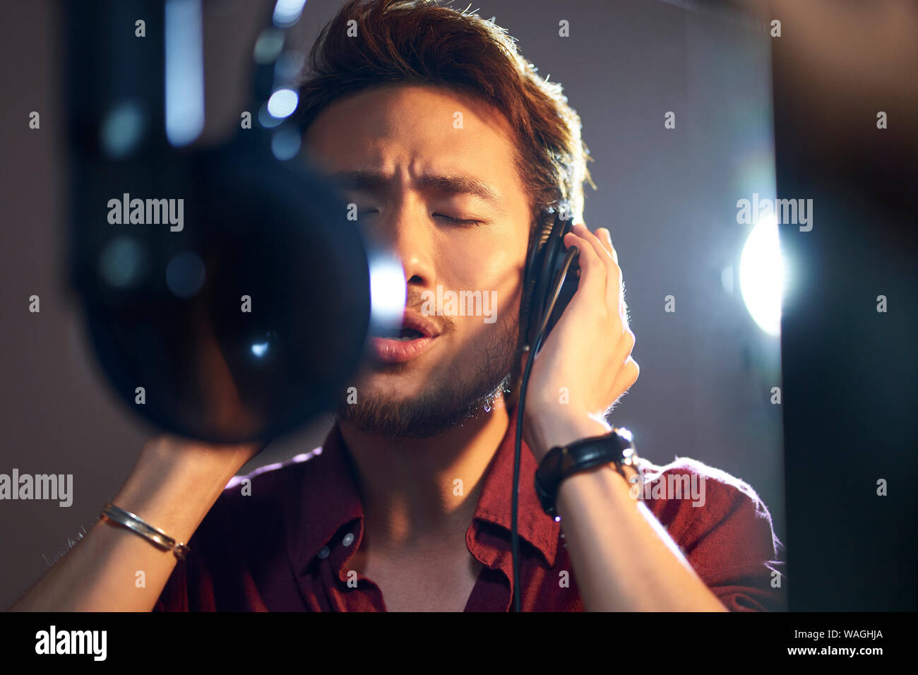 Hombre adulto joven asiático disfrutar cantando una canción en estudio de grabación moderna Foto de stock