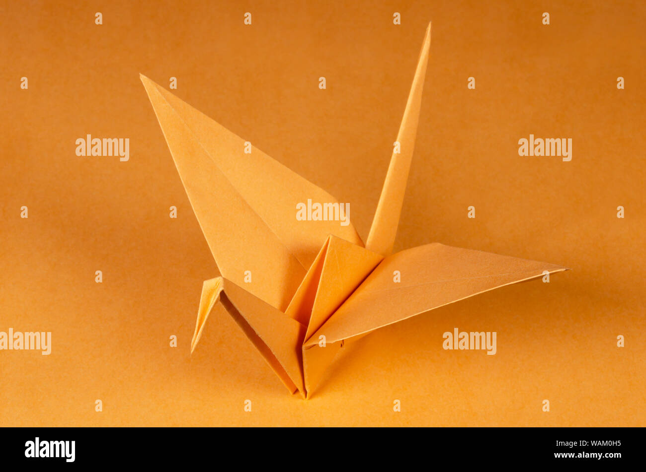 Grúa origami naranja sobre fondo naranja. Tsuru. Arte japonés de plegado de papel. Hoja de papel cuadrado plano trasladados en una escultura terminada. Foto de stock
