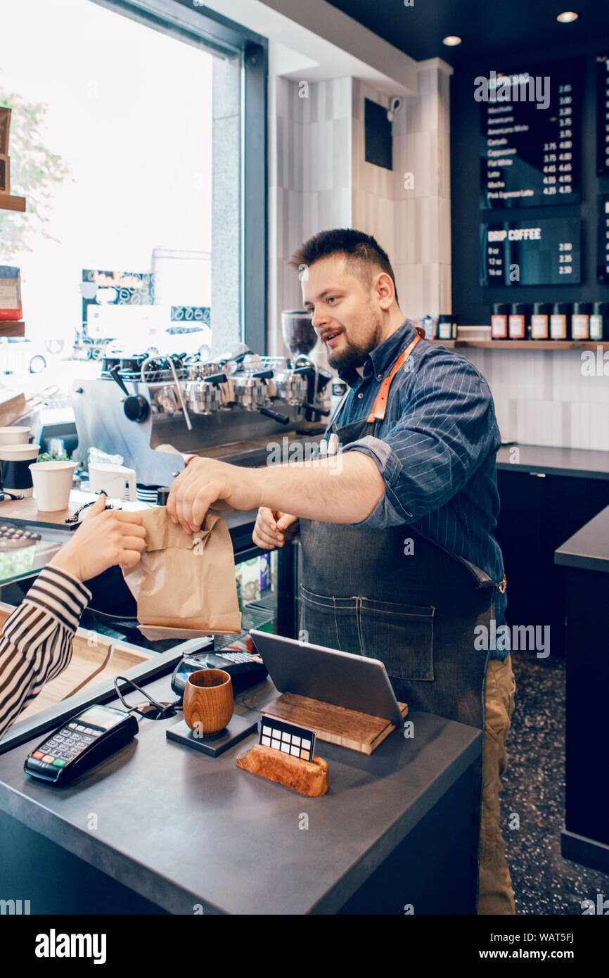 Sonriente barbudo hombre caucásico barista cajero en el restaurante Cafe en  el trabajo. Vendedor dando al cliente su compra alimentos en papel orgánico  packa marrón Fotografía de stock - Alamy