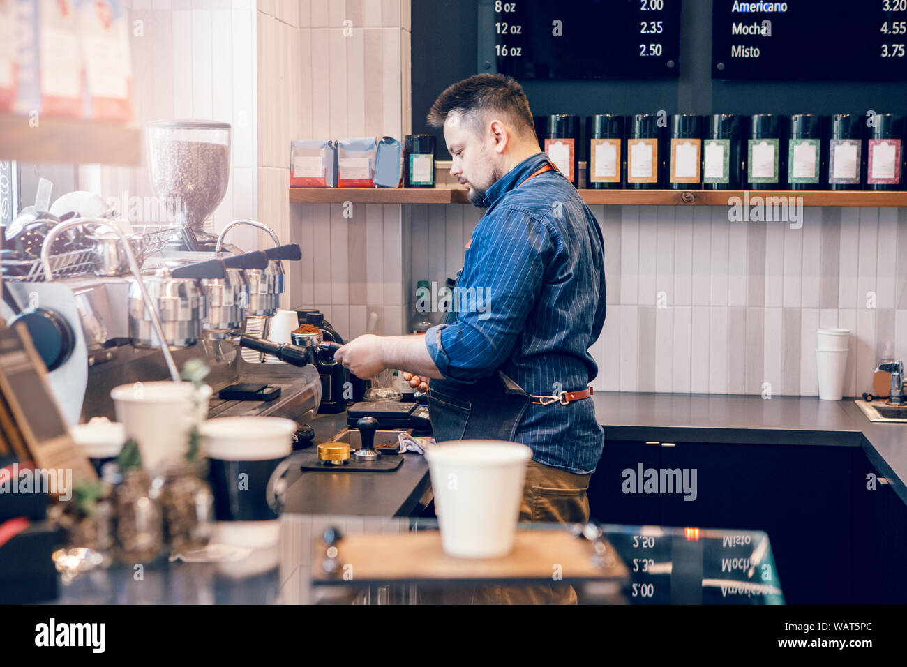 Hombre caucásico barista haciendo espresso cappuccino bebida caliente. Camarero empleador cocinar en cafe bar restaurante. Concepto de negocio local pequeño. Interior des Foto de stock