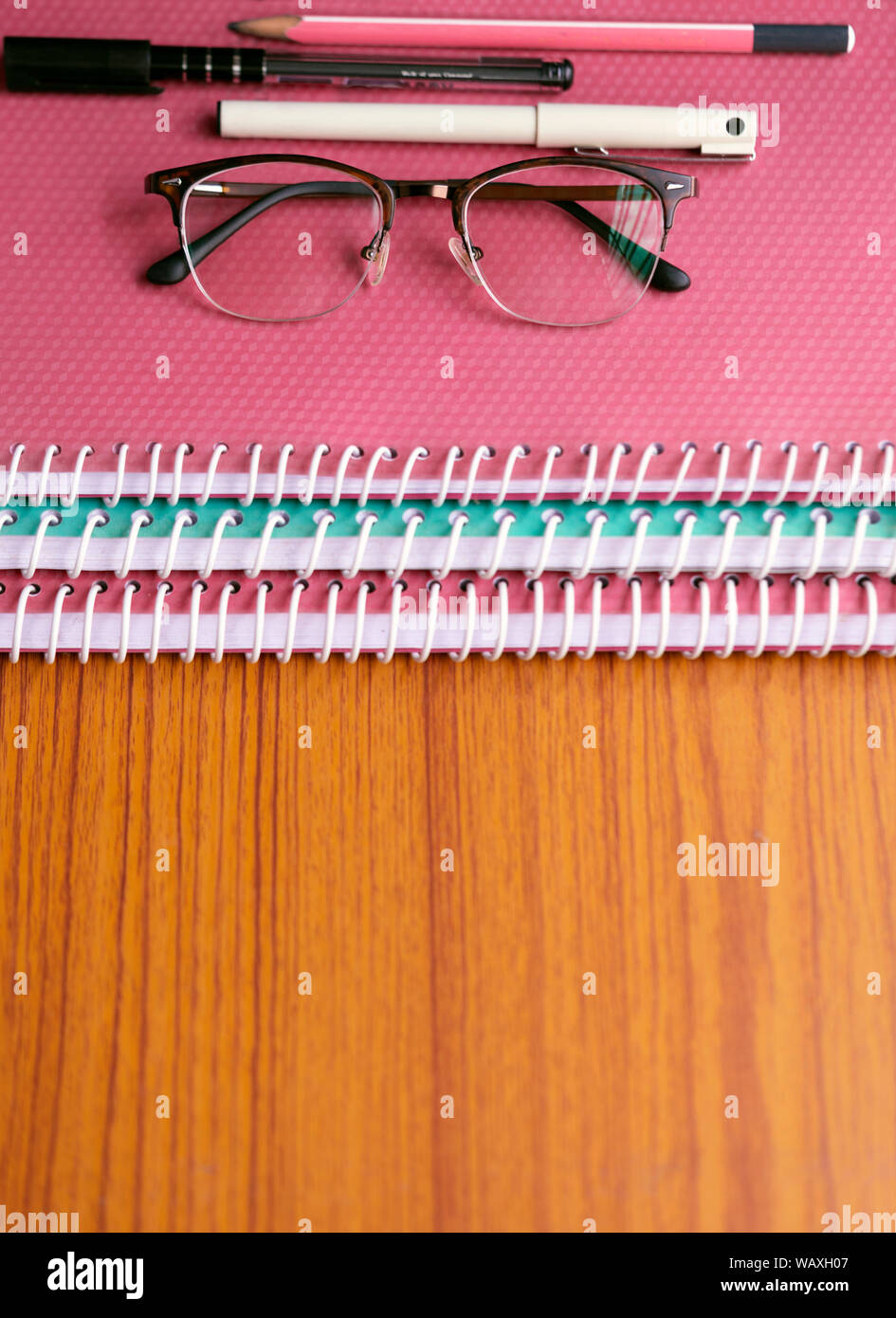 Los libros y las asignaciones con las gafas del profesor, bolígrafos y escala apiladas sobre un escritorio de madera con espacio para texto o copia. Concepto de educación infantil, sc Foto de stock
