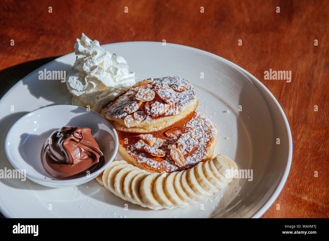 Esponjosos panqueques con salsa de chocolate almendras horneadas montar  nata y plátano en la placa blanca sobre la mesa de madera bajo la luz solar  Fotografía de stock - Alamy