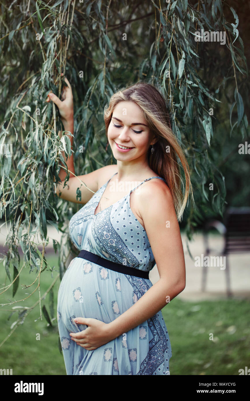 Feliz saludables durante el embarazo y la maternidad. Retrato de mujer caucásica joven embarazada vestidos de largo vestido azul posando en el parque afuera. Hermosa pensive fe Fotografía stock - Alamy