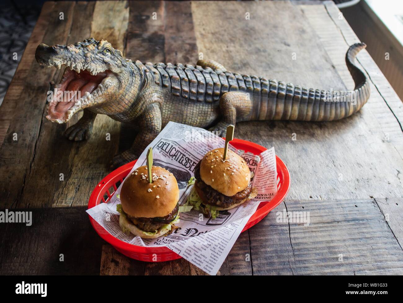 Cerca de un tiro de hamburguesas en una bandeja roja cerca de un juguete de  cocodrilo sobre una mesa de madera Fotografía de stock - Alamy