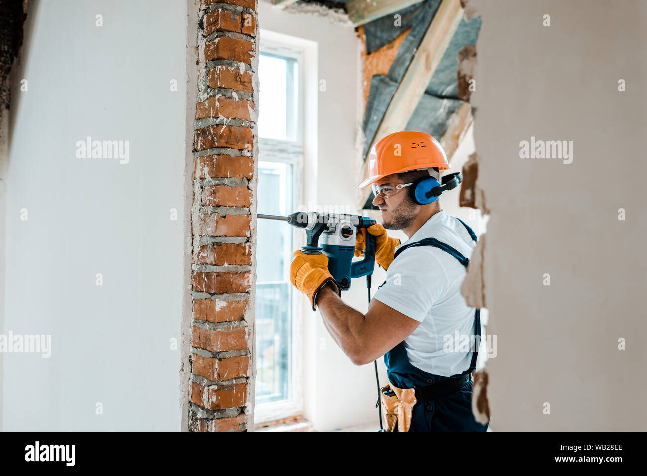 El enfoque selectivo de obrero en uniformes y guantes amarillos con taladro  de martillo en la pared de ladrillo Fotografía de stock - Alamy