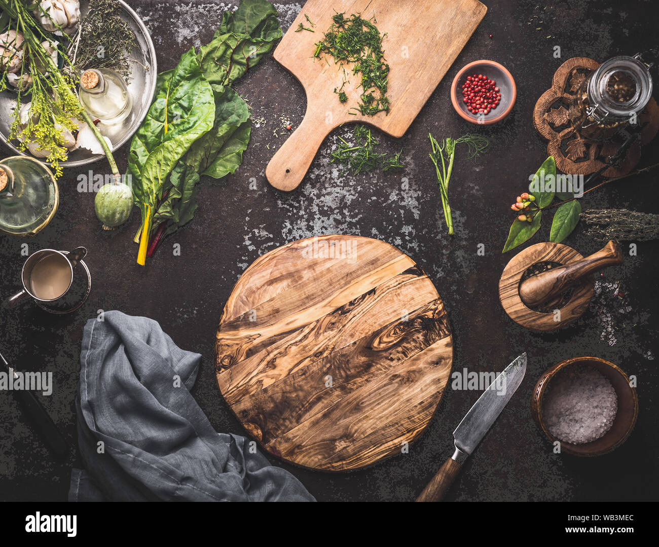 Comida vegetariana cocina fondo con hojas de acelga , especias y utensilios  de cocina en torno a un círculo vacío en la tabla de cortar de madera  oscuro fondo rústico Fotografía de