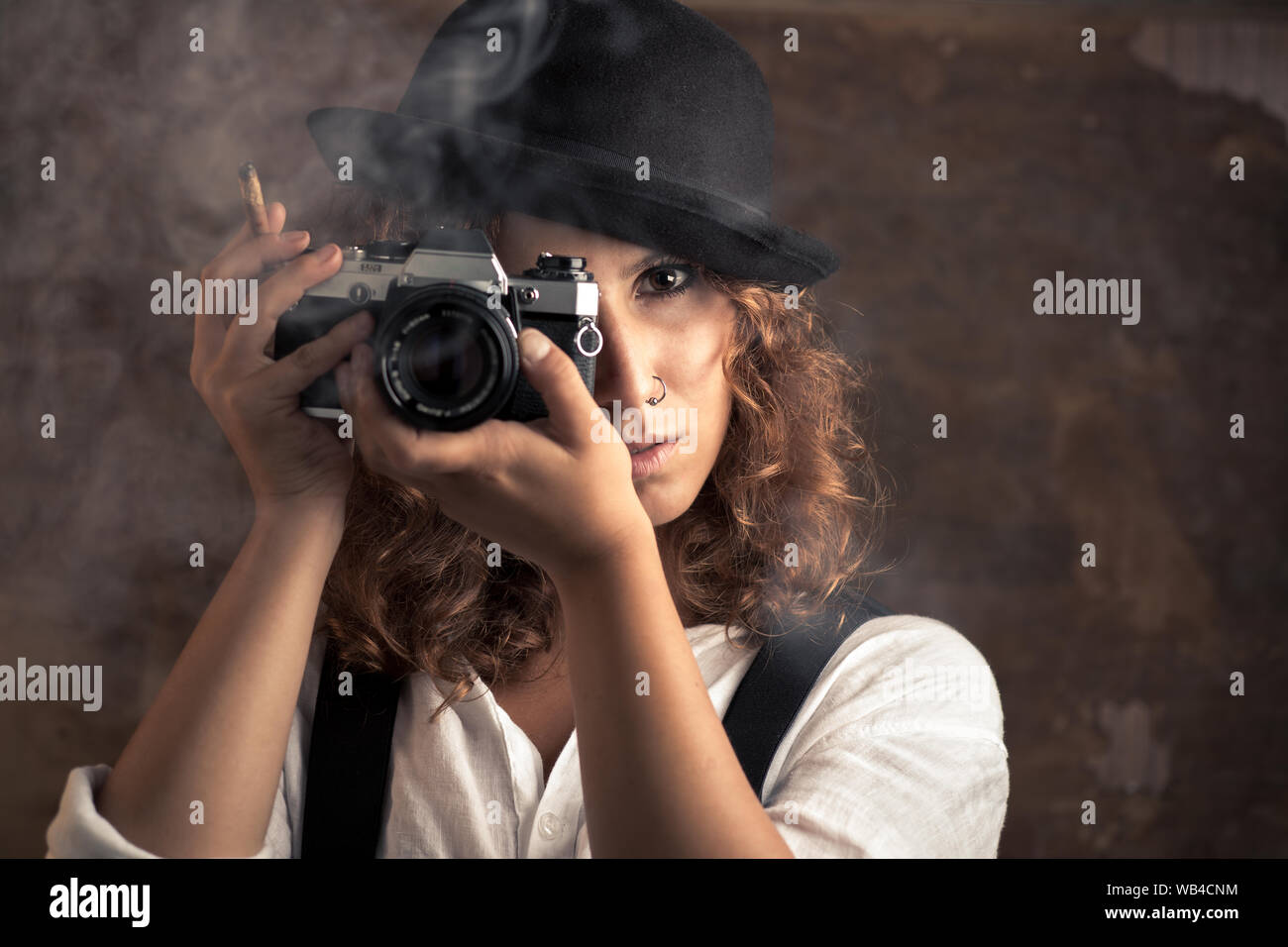 Mujer fotógrafo con Bowler y tirantes sujetando un cigarro Foto de stock