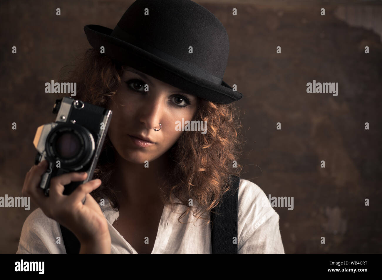 Mujer fotógrafo con Bowler y tirantes sujetando una cámara Foto de stock