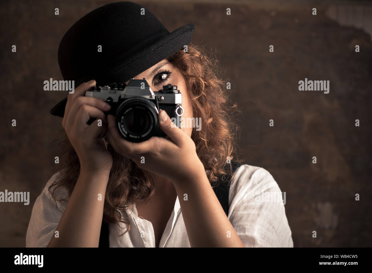 Mujer fotógrafo con Bowler y tirantes sujetando una cámara Foto de stock