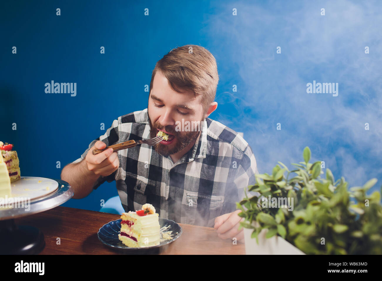 La gente, el ocio, el concepto de alimentos - apuesto hombre sonriente con  la camisa blanca sentado en una mesa comiendo su desayuno. El desayuno por  la mañana - hombre barbado comiendo