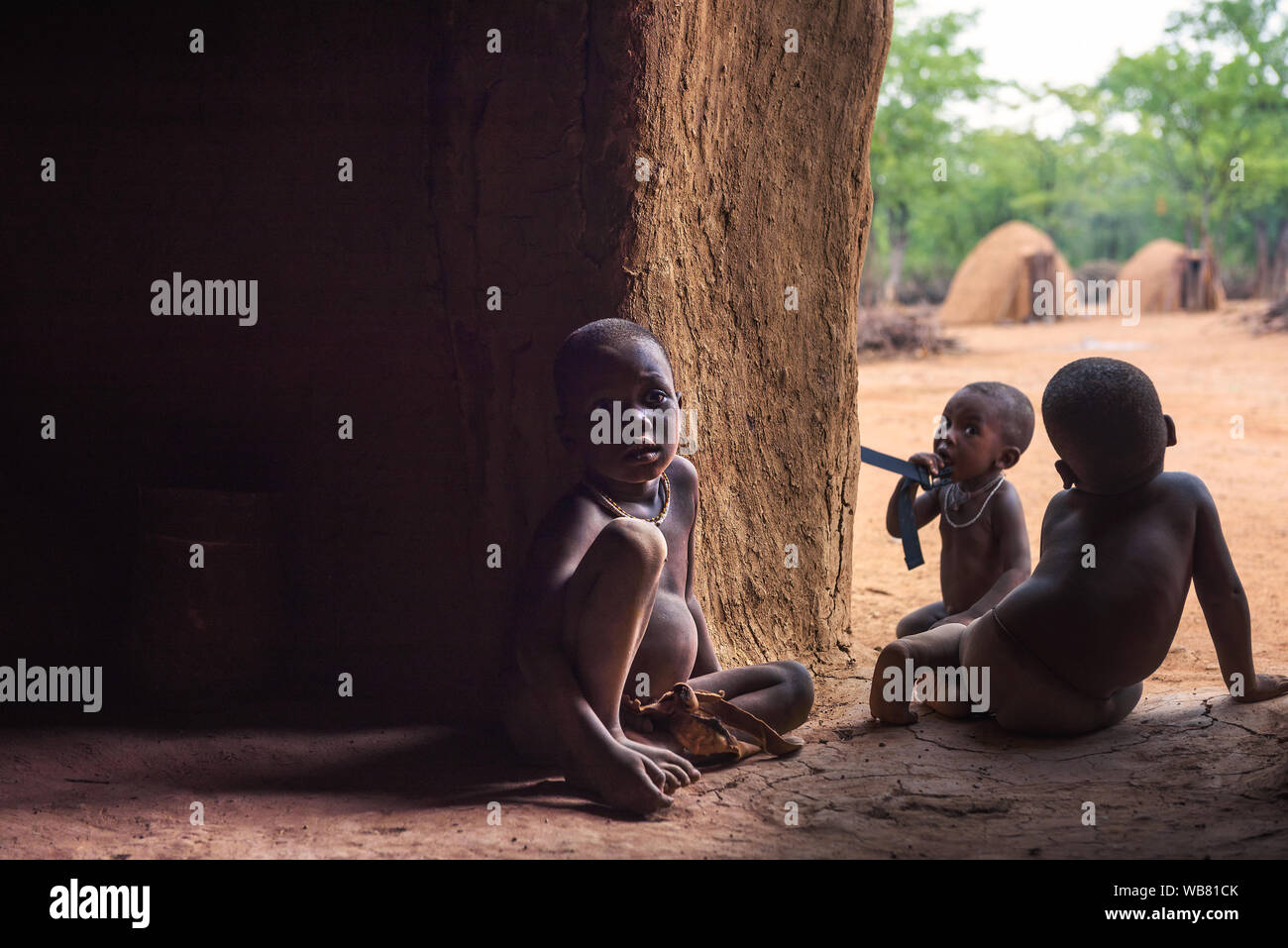Tres niños de la tribu Himba en Namibia juegan en su cabaña Foto de stock