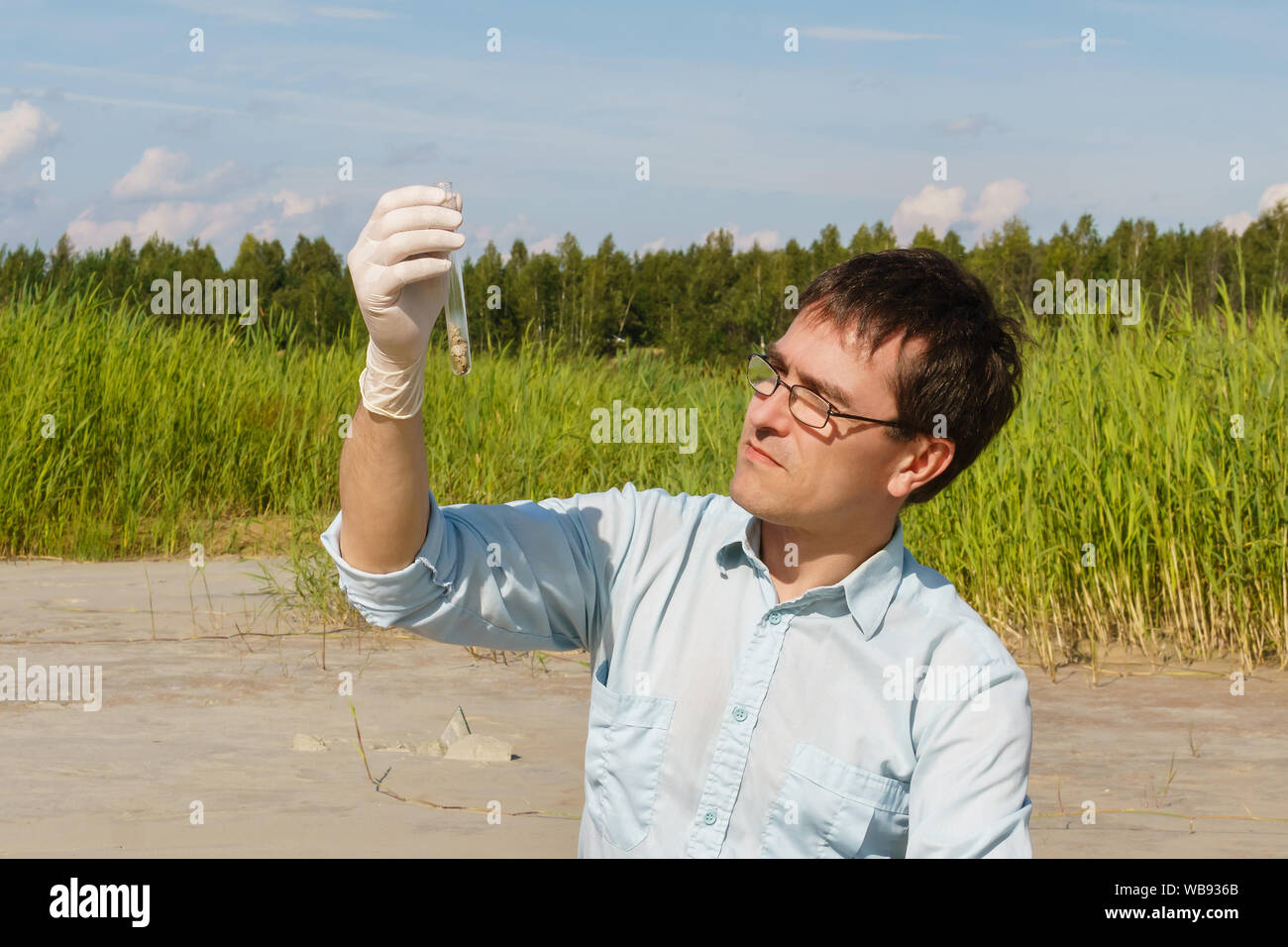 Hombre ecologista ni biólogo examina una muestra de suelo en un tubo de ensayo contra un pantano seco Foto de stock