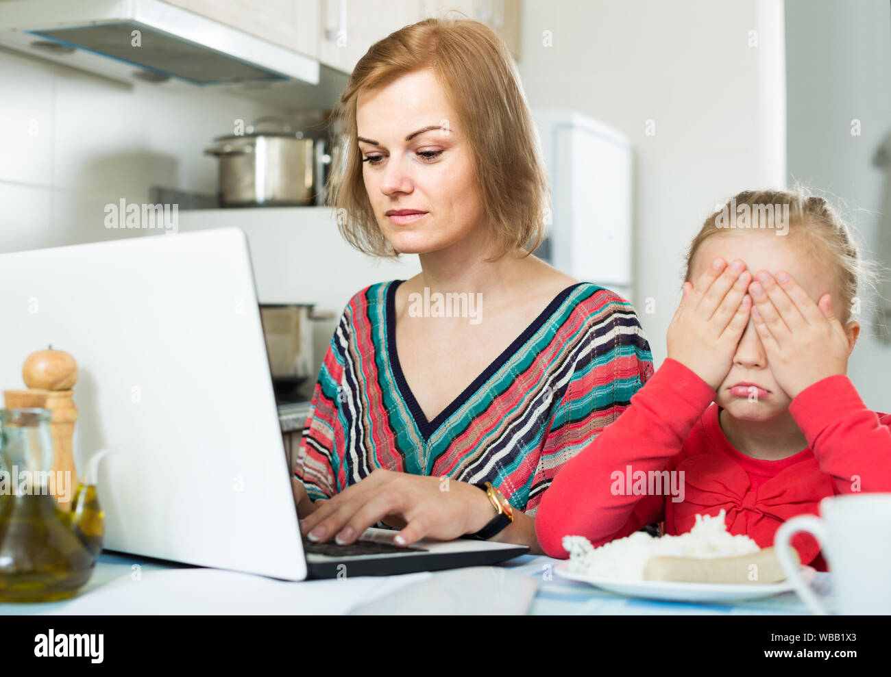 American Woman ocupada trabajando desde casa, pequeña hija pidiendo atención Foto de stock