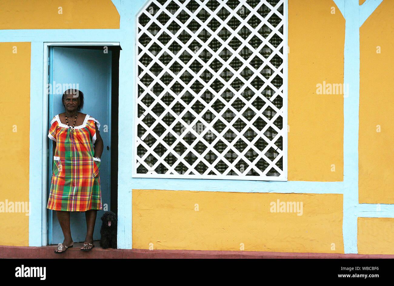 El Cayenne, Guyana Francesa - 7.30.2010 - mujer negra en vestimentas tradicionales de pie en la puerta de una casa amarilla Foto de stock