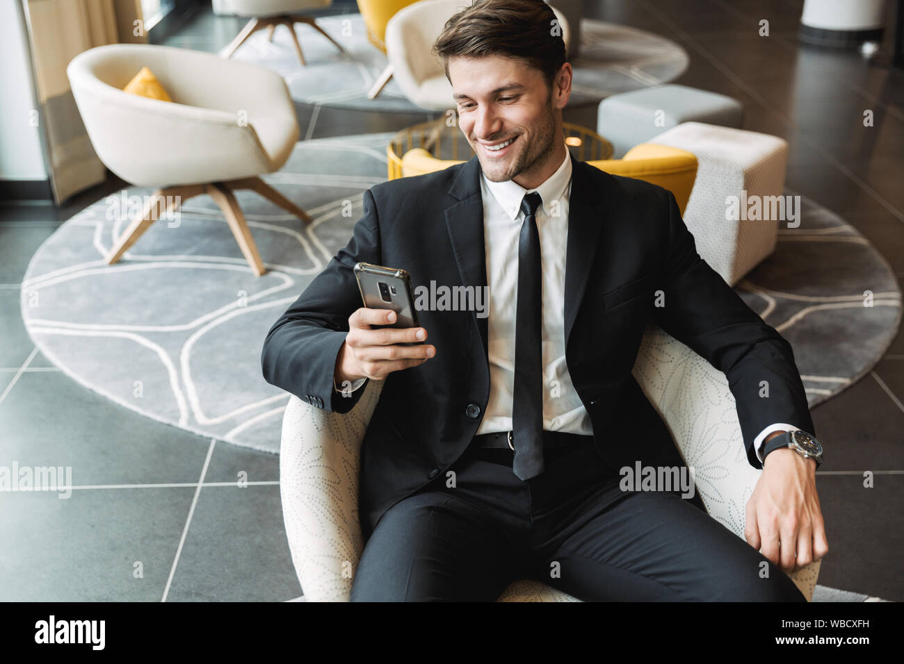 Foto de la hermosa joven hombre vestido con traje negro formal sentados en  el pasillo del hotel con el smartphone durante un viaje de negocios  Fotografía de stock - Alamy