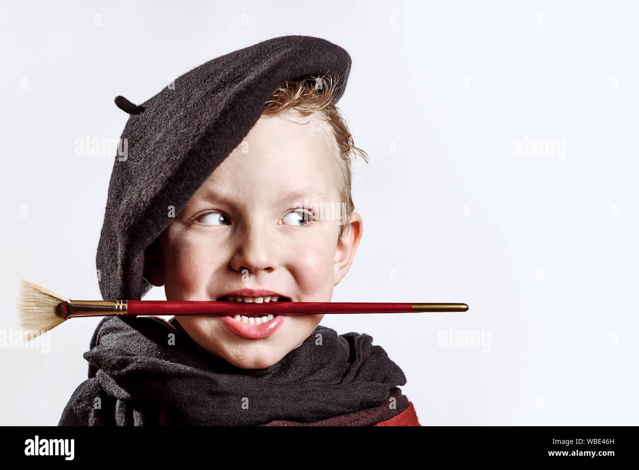 leninismo golpear preámbulo Niño alegre artista boina negra, bufanda y con un pincel en su boca sobre  un fondo de luz Fotografía de stock - Alamy