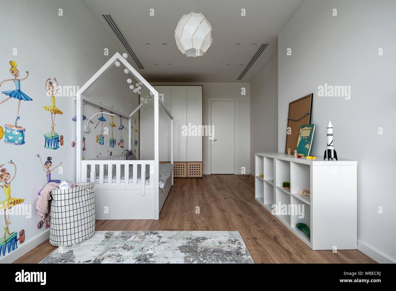 Habitación infantil contemporáneo con paredes blancas con coloridas imágenes y un parquet moqueta en el suelo. Hay una cama, estanterías con libros y juguetes Fotografía de stock - Alamy