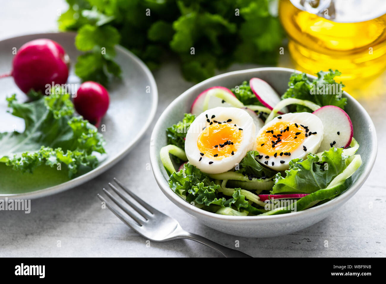 Con ensalada de pepino, rábano, huevo duro y Kale en un tazón vestida con aceite de oliva. Visión más cercana. Comer una dieta saludable, concepto Foto de stock