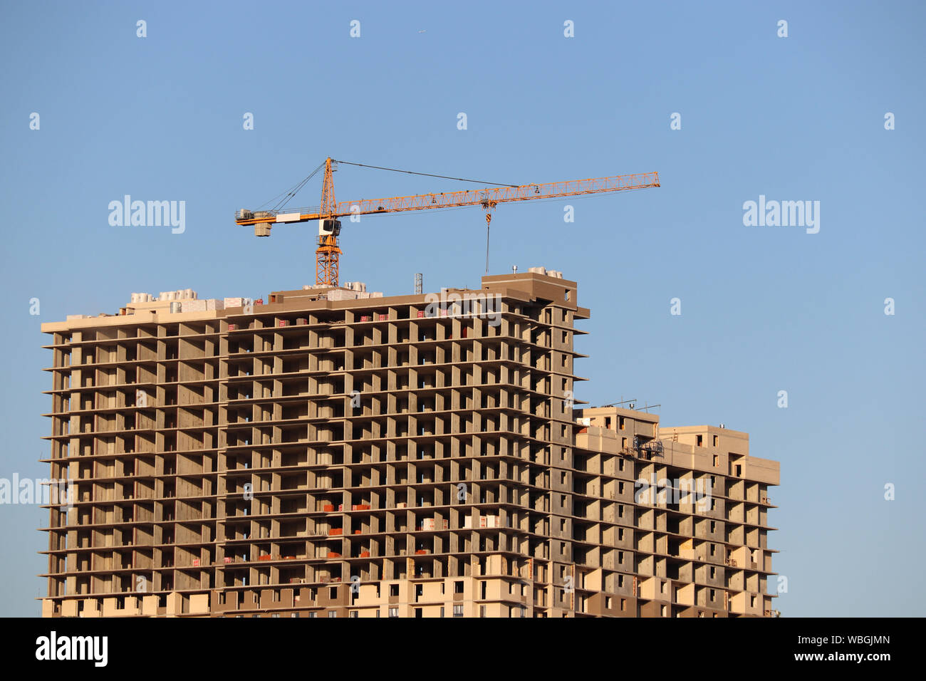Grúa de construcción e inconclusa de alto edificio residencial sobre fondo de cielo azul claro Foto de stock