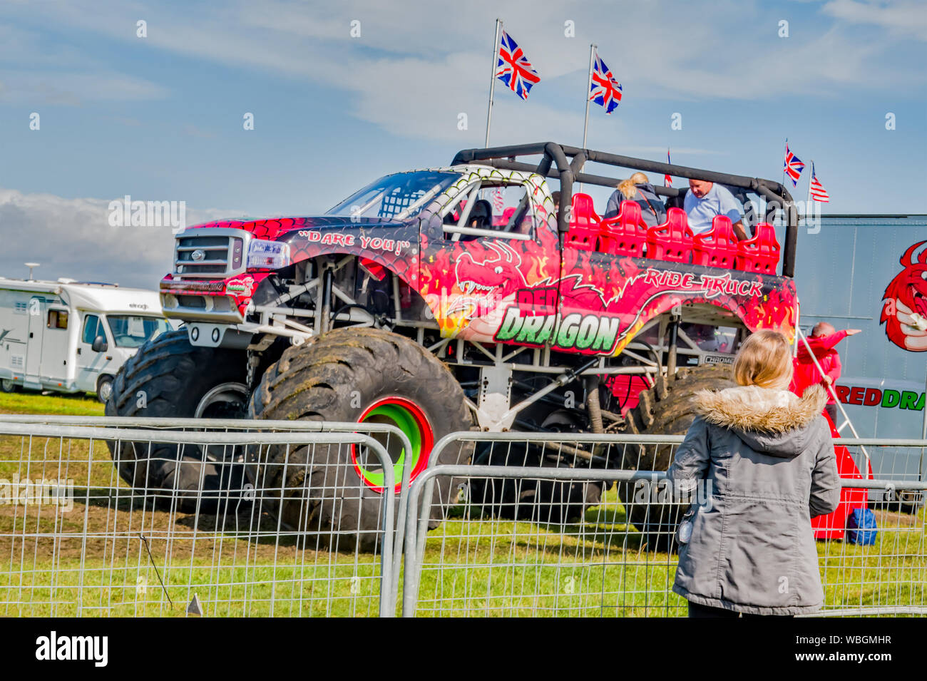 Una joven madre de pie detrás de la barrera de seguridad mirando a su esposo e hijo a bordo del dragón rojo monster truck para un paseo en Santa Pod franja de arrastre Foto de stock