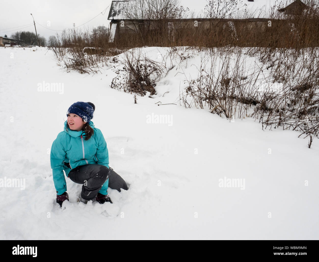 Linda chica de rodillas en el campo cubierto de nieve en invierno Foto de stock