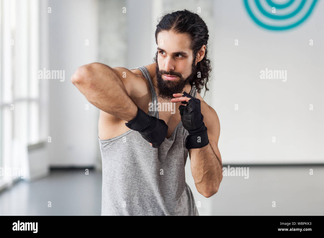 Retrato de un hombre adulto joven muscular enojados con el cabello rizado y preparación permanente para luchar con el codo en guantes negros, mostrando kickboxing profesional Foto de stock