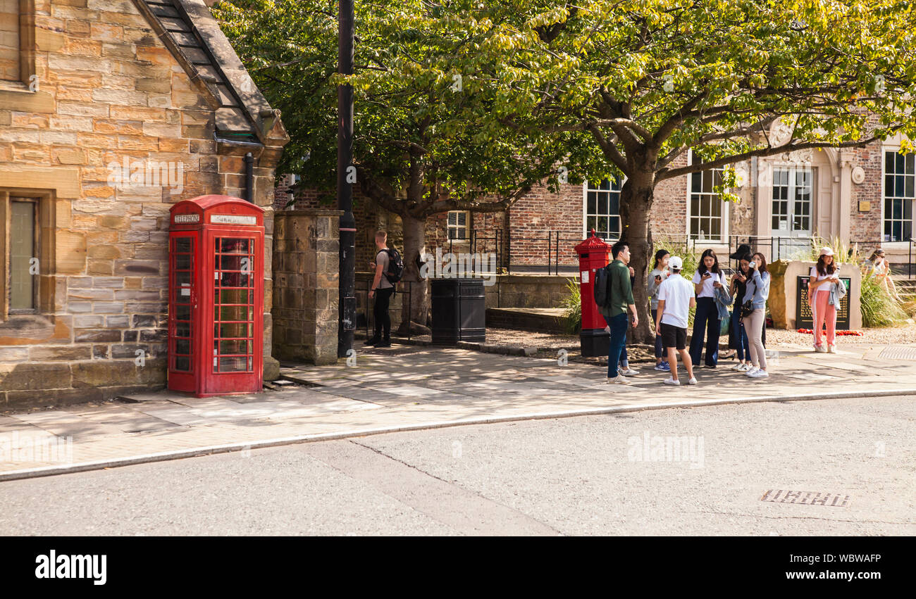 Una escena callejera en Durham con estudiantes asiáticos conversando junto a un cuadro de teléfono rojo Foto de stock