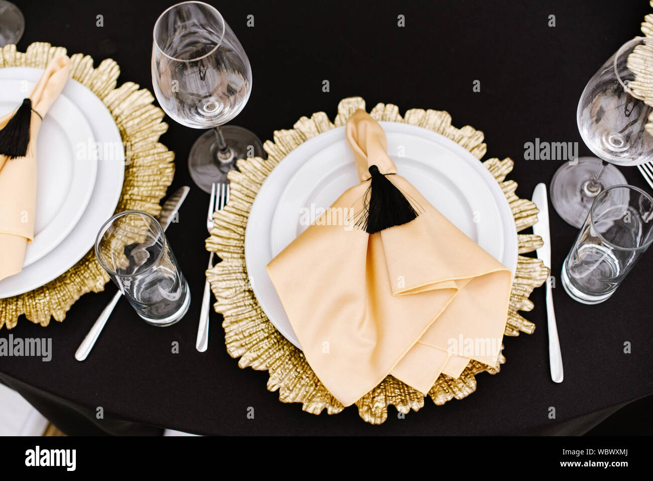 Un comedor, una placa blanca y una decoración de plato de metal dorado  sobre la mesa en el restaurante. Una servilleta de tela hecha de golden  atlas y pincel negro Fotografía de