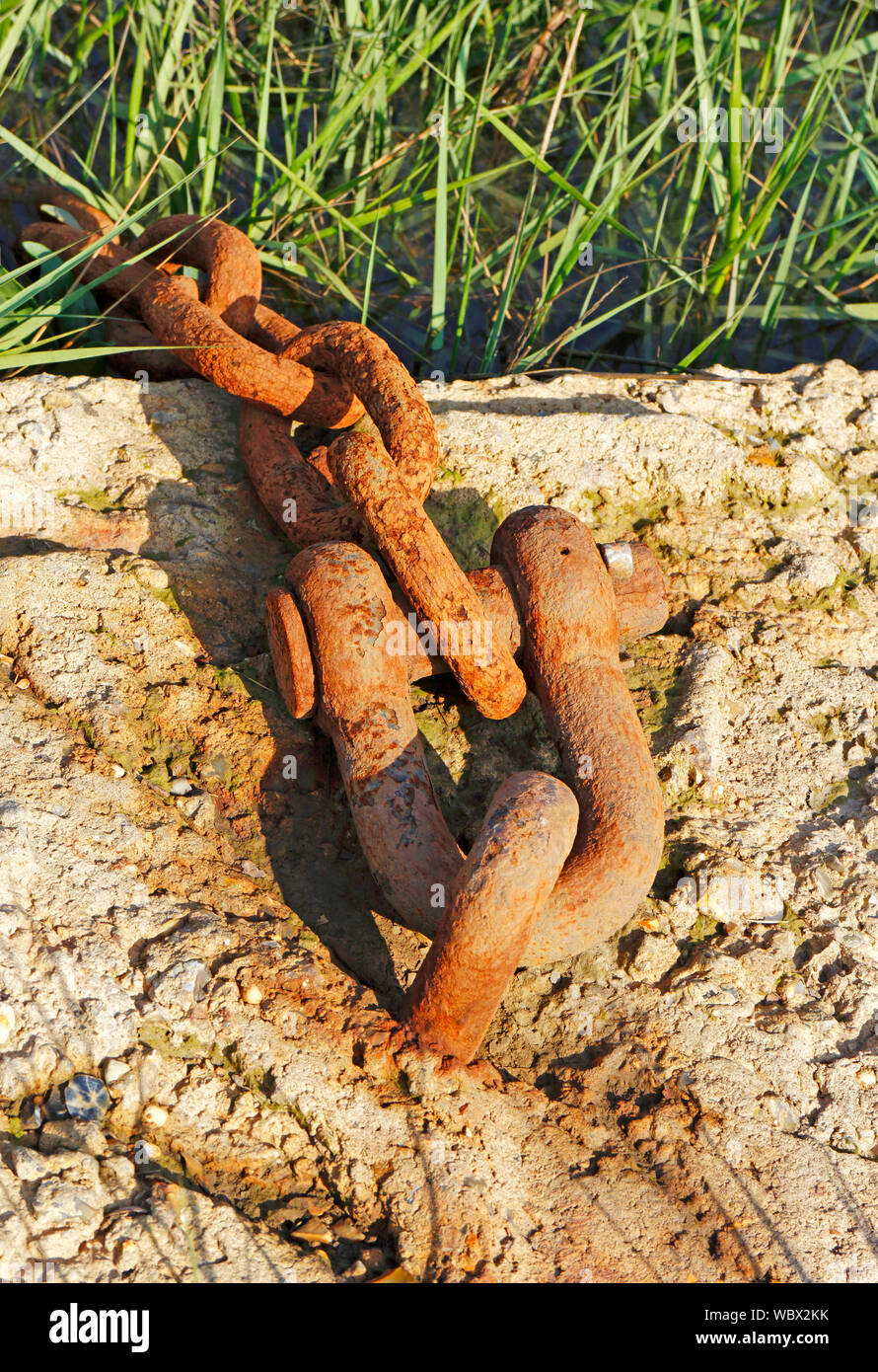 Una pesada cadena oxidados en un bloque de cemento utilizado como un barco a punto de amarre pozos junto al mar, Norfolk, Inglaterra, Reino Unido, Europa. Foto de stock