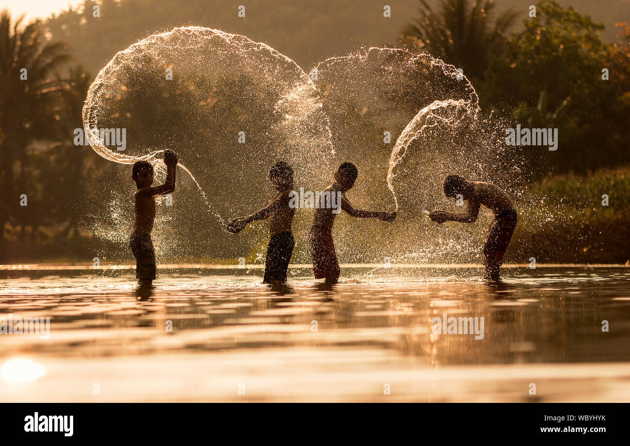 Vista lateral de amigos varones salpicaduras de agua en el lago al atardecer. Foto de stock