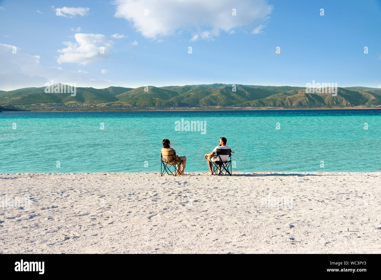 Salda lago como Maldivas, con arenas blancas y aguas color turquesa. Una pareja sentados en sillas portátiles cerca de la orilla del agua. Burdur / Turquía. Foto de stock