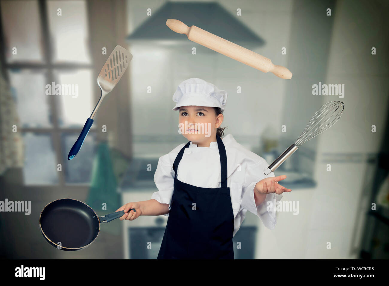 Chica en Chef blancos jugando con utensilios de cocina. Foto de stock