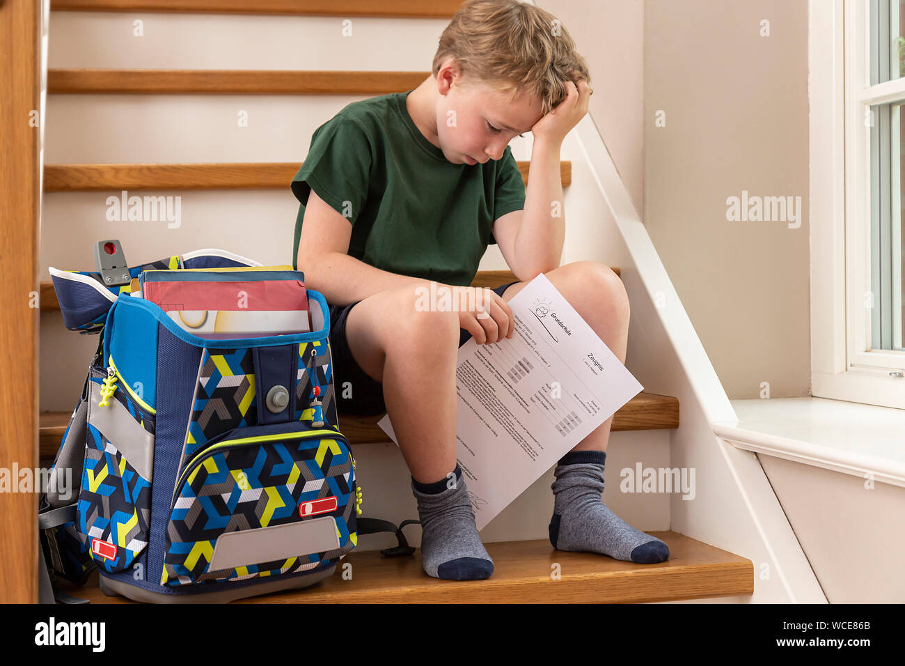 Disppointed boy, de 8 años, en su casa con su informe de la escuela primaria. Foto de stock