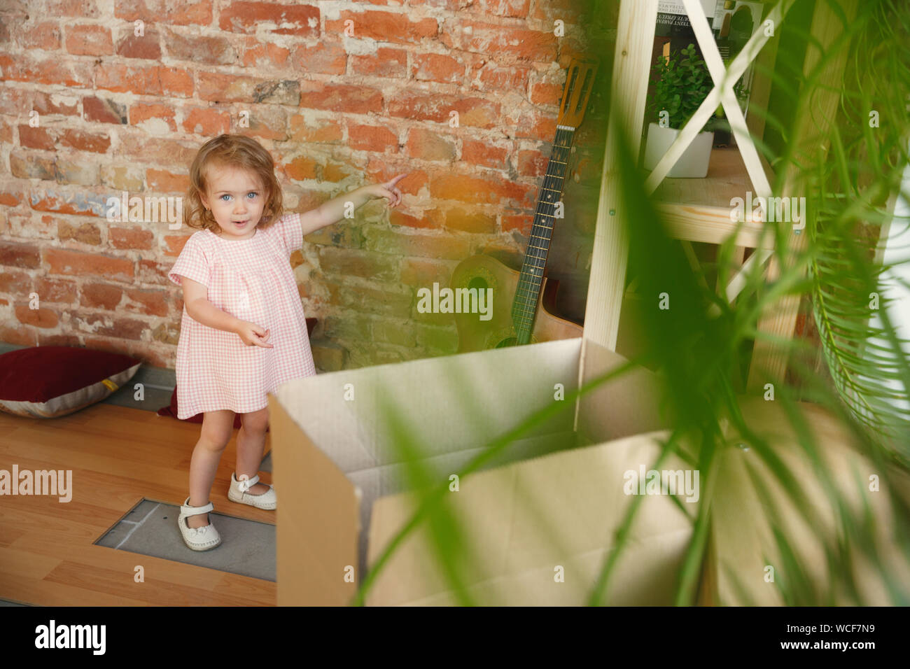 Nueva vida. Cute Little Girl se mudó a una nueva casa o apartamento. Parecen felices y seguros. En movimiento, las relaciones, el concepto de estilo de vida. Descubriendo su nuevo salón para niños, señalando la pared de ladrillo, sonriendo. Foto de stock