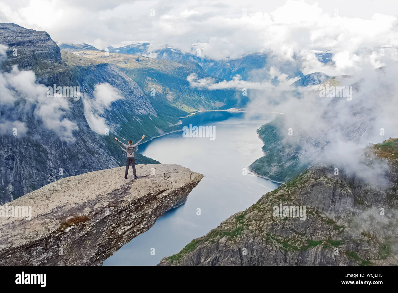 Joven viajero parado en el famoso espectáculo natural noruego Trolltunga con sus manos se levantaron tras la larga caminata Foto de stock
