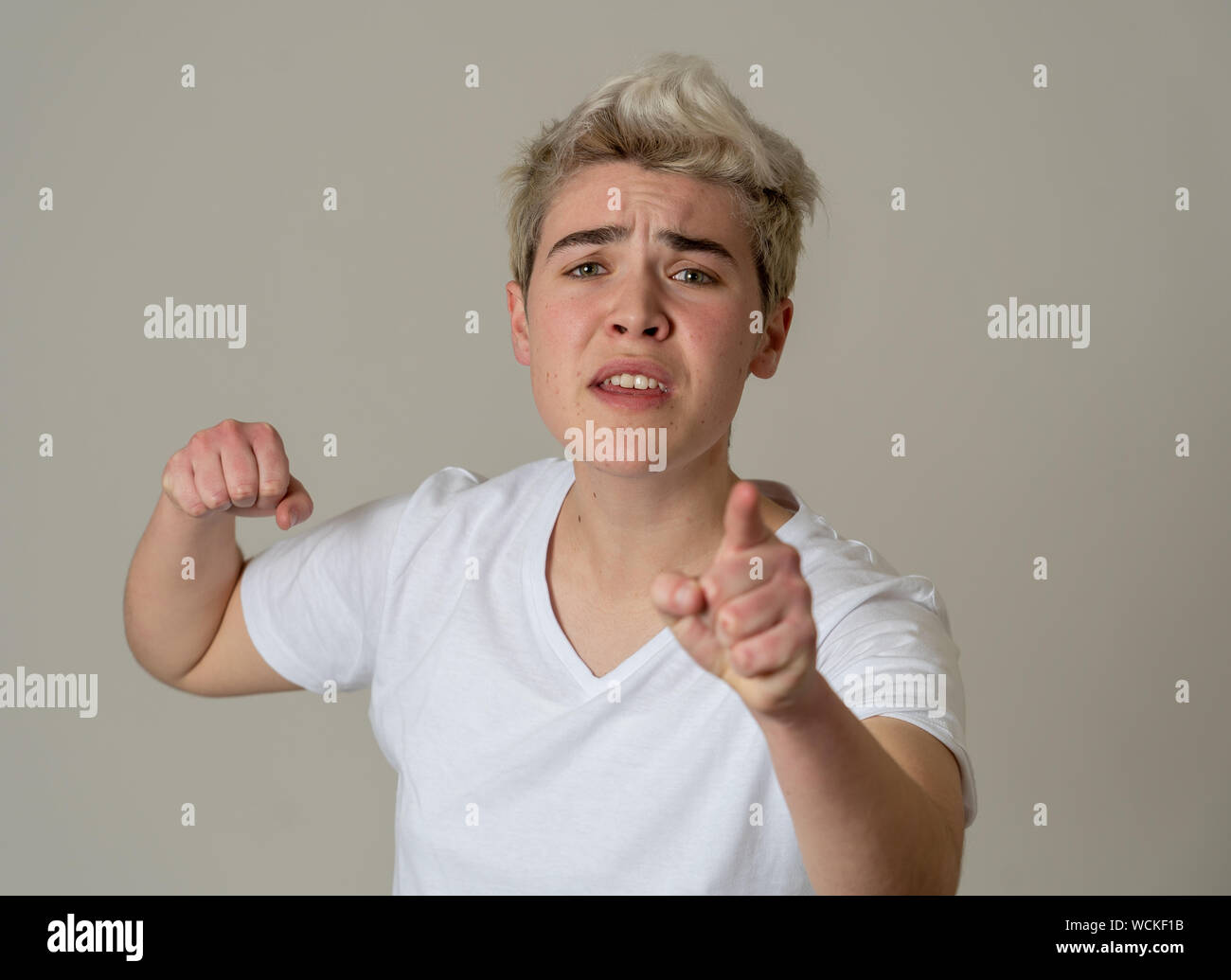 Retrato de joven adolescente transgénero atractivo hombre con enojo. Mirando enojado y furioso. Las expresiones faciales y emociones. Aislado en punto muerto b Foto de stock