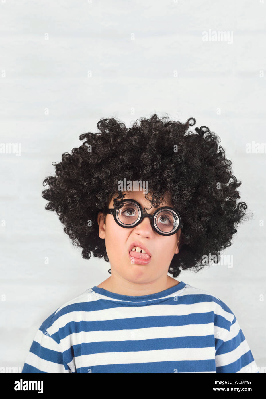 Gracioso niño haciendo una mueca llevaba gafas nerd sobre fondo de ladrillo Foto de stock