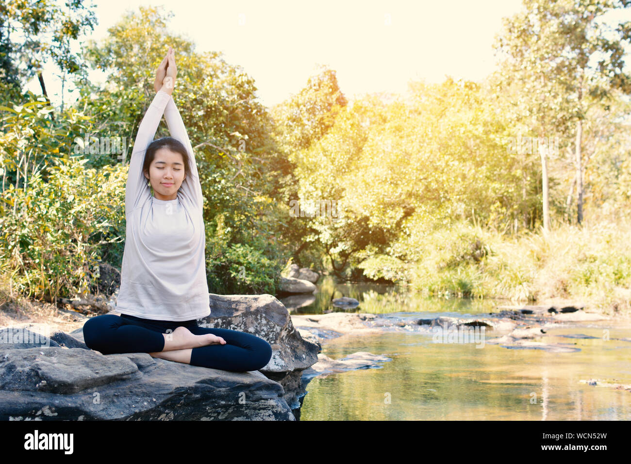Vista frontal de la mujer practicando Yoga en roca por el río Foto de stock