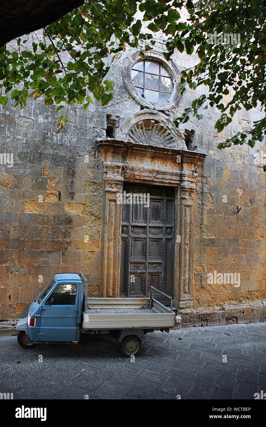 Puerta renacentista de la pequeña iglesia de San Dalmazio, y una de tres ruedas Piaggio Ape, Via San Lino, Volterra, Toscana, Italia Foto de stock