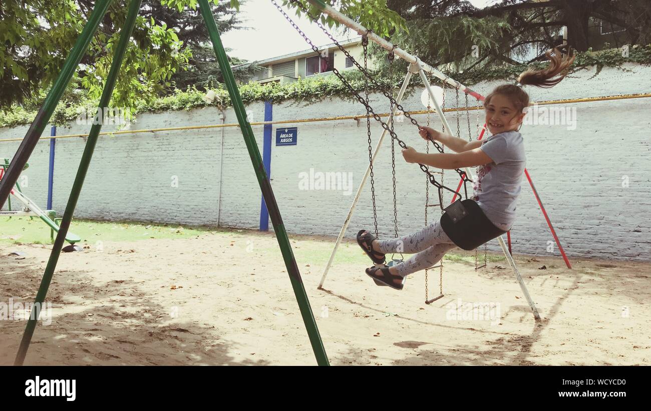 Retrato de longitud completa de la alegre niña balanceándose en Playground Foto de stock