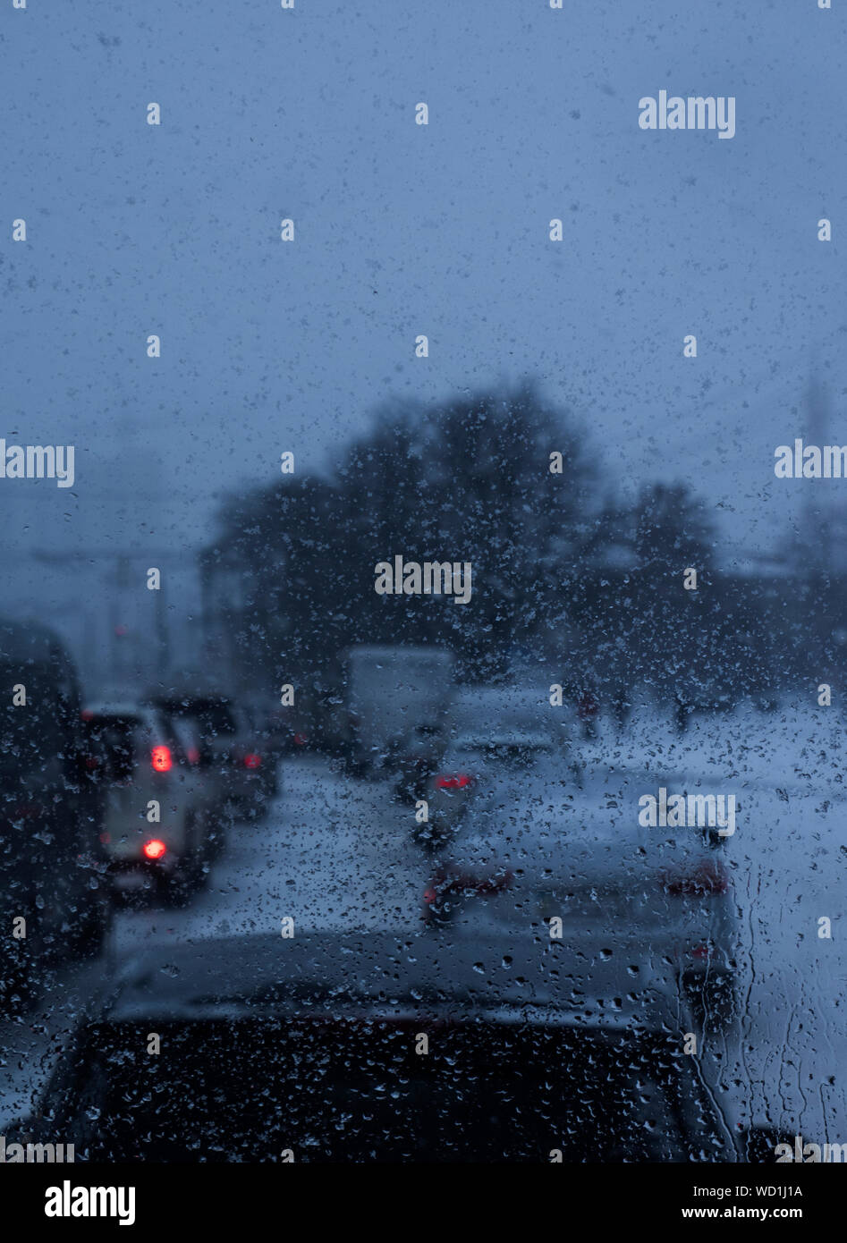 Coches en el tráfico vistos a través del parabrisas mojado al anochecer durante el invierno Foto de stock