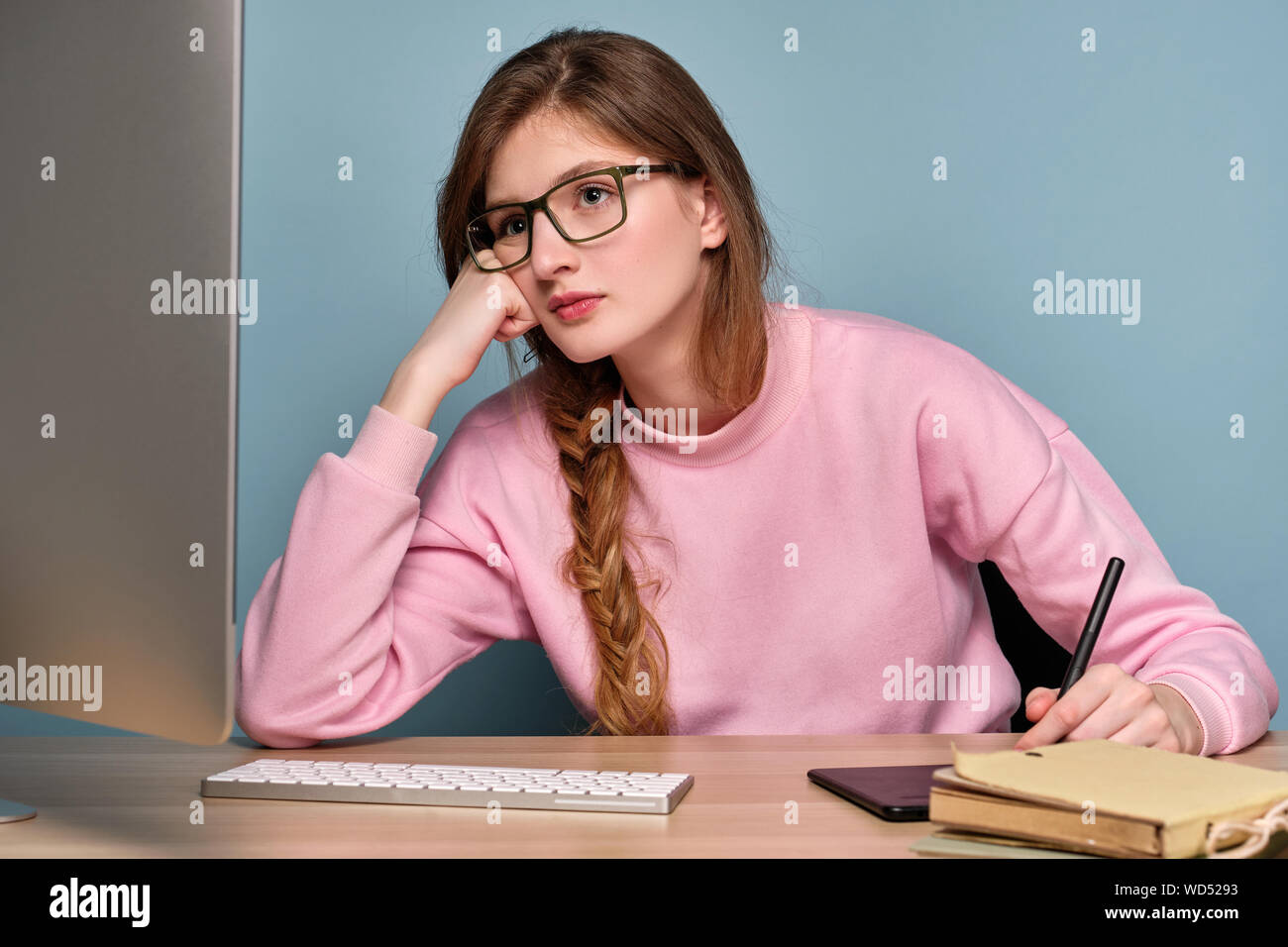 Una chica en un suéter rosa y gafas se asienta en un ordenador y se ve en  el monitor con su puño apoyada en su mejilla Fotografía de stock - Alamy