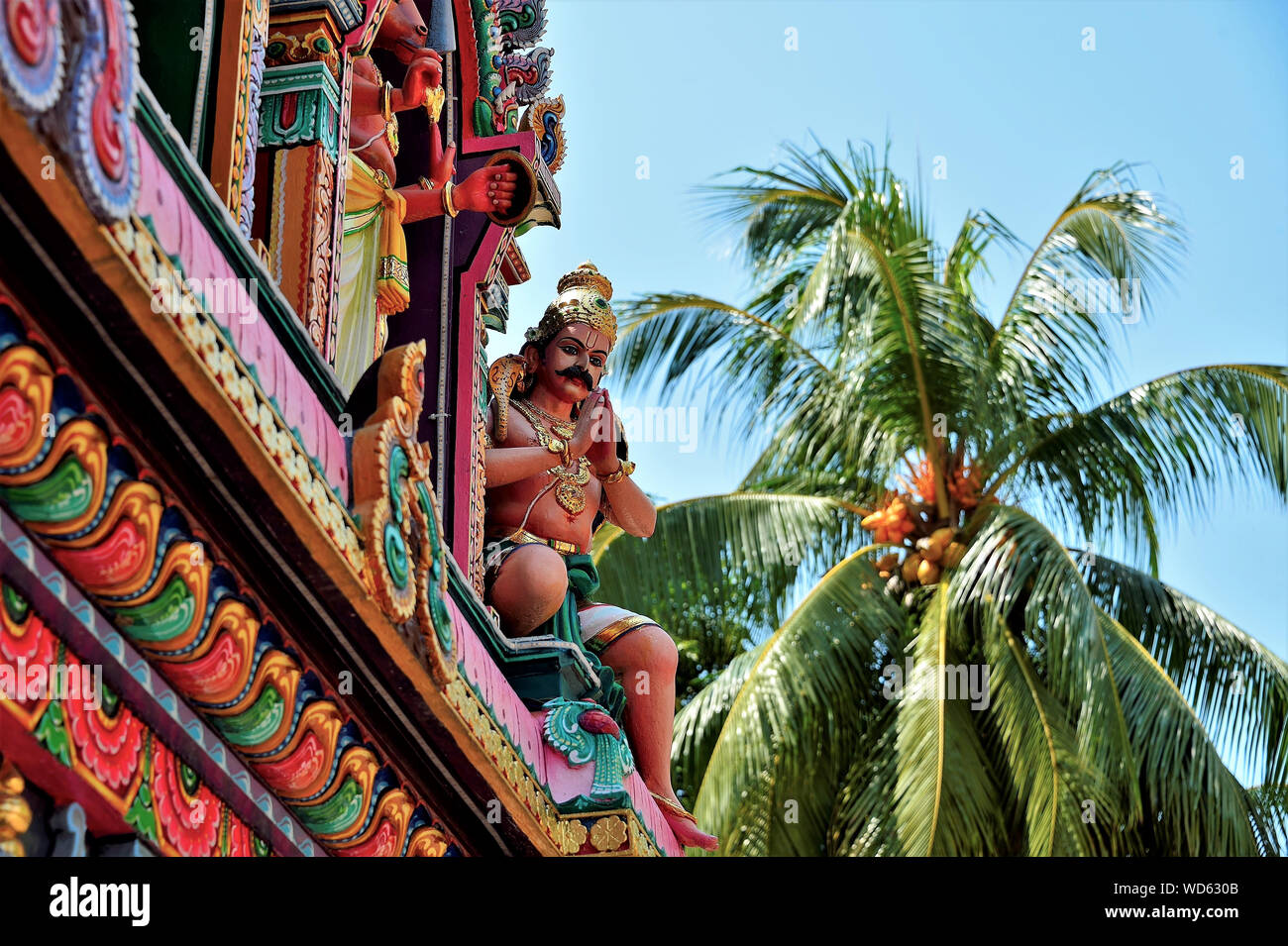 Estatua de piedra de la deidad hindú hindú en la oración en el lado de la pared del templo colorido con palmera en soft focus antecedentes Foto de stock